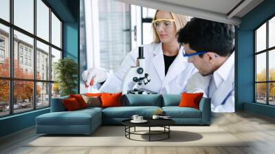 Scientists checking medical liquid with microscope while doing health care research in laboratory Wall mural