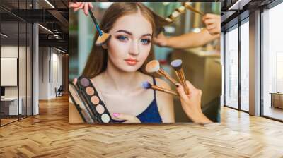 Portrait of the happy young woman who is sitting indoors and makeup artist doing makeup her and hairdresser doing the hairdo her Wall mural