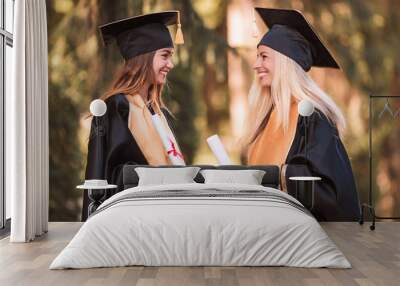 side view of two young happy joyful graduates in mantles who standing outdoor and keeping diplomas i Wall mural