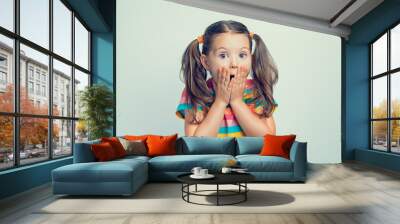 shocked or surprised beautiful cute little girl closing her mouth with hands Wall mural