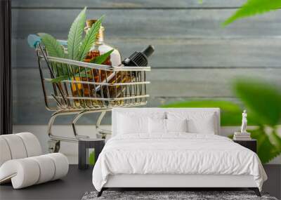 Supermarket trolley with marijuana leafs and medical cannabis oil cbd on wooden backdrop Wall mural