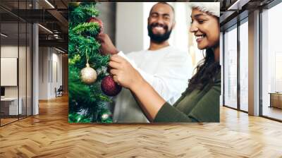 Christmas, love and couple decorating Christmas tree together for holiday, festival celebration and vacation. Bonding, marriage and happy man and woman decorate tree for festive tradition at home Wall mural