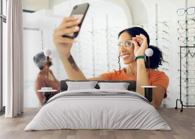 Selfie, optometry and woman trying glasses with prescription lenses and frame in an optical store. Vision, smile and young female person taking a picture on a phone for choosing spectacles in clinic. Wall mural