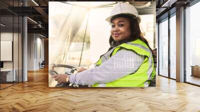 Forklift driver, black woman and logistics worker in industrial shipping yard, manufacturing industry and transport trade. Portrait of cargo female driving a vehicle showing gender equality at work Wall mural