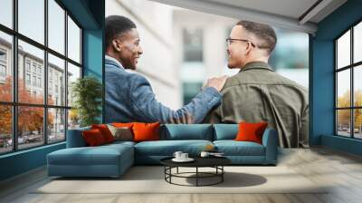 Two young businessmen smiling, talking and walking through the city together, excited for their new project. Happy multiracial coworkers strolling with his hand on his friends shoulder while laughing Wall mural