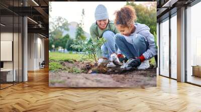 Volunteer, child and woman with plant for gardening in park with trees in nature environment. Happy family team helping and planting for growth, ecology and sustainability for community on Earth day Wall mural