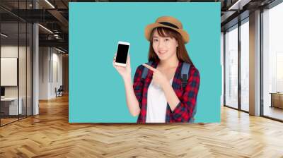 Beautiful young asian woman showing smart mobile phone for presenting and pointing something in travel summer trip in vacation isolated on blue background, asia girl holding smartphone. Wall mural