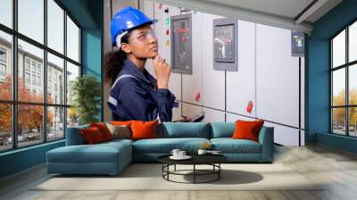 Electrical young asian woman engineer examining maintenance cabinet system electric and using tablet in control room at industrial factory, technician or electrician inspection power distribution. Wall mural