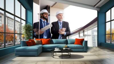 Senior architect inspector talking with contractor man together at office while holding blueprint building structure, executive and engineer planning project, industry and construction concept. Wall mural