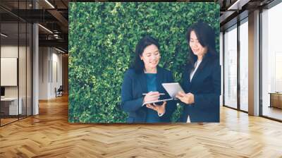 Two business people discussing information on a tablet-and taking notes as they work together as a team in the garden. Wall mural