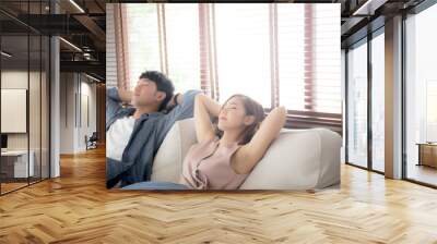 Young asian couple smile relax comfortable on sofa in the living room in holiday, family leisure and resting with happy in vacation on couch at home, lifestyle and wellbeing concept. Wall mural