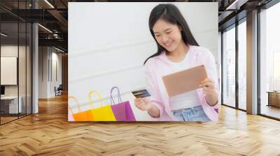 Young asian woman sitting on sofa using digital tablet shopping online with credit card while paper bag on couch, female paying with transaction financial, purchase and payment, business concept. Wall mural