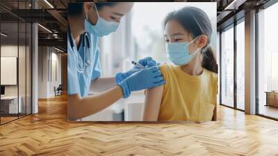 A healthcare professional administers a vaccine to a young girl wearing a yellow shirt, both wearing masks for safety. Wall mural