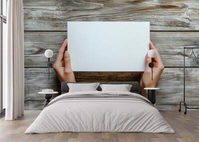 Two hands holding a blank piece of paper against a rustic wooden background, ready for text or artwork. Wall mural