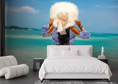 Beautiful lady in a striped T-shirt and denim shorts, sunglasses and a straw hat. Positive emotions. Embankment on the background of the sea. The concept of summer holidays, relax, travel Wall mural