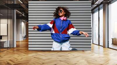 Cool black girl with curly hair, glasses, 90s, 80s, retro hip hop style, dancing against a metal wall, dynamics and expression Wall mural