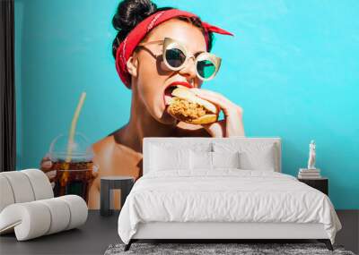 Merry amazing girl eats fast food, drink sodas, eat burger, close-up portrait, tasty bites burger, a stylish makeup and hairstyle after the barber shop, a bright pink background, a bandage on his head Wall mural