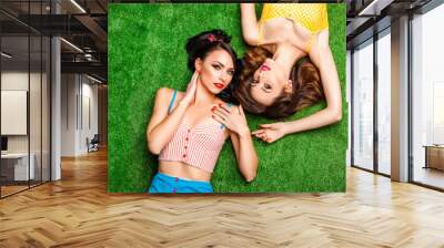 Two bright girls in the style of pin-up smile lie on artificial grass in the studio Wall mural