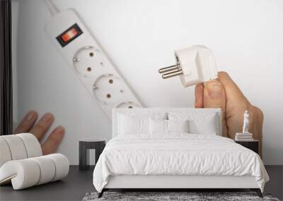 a hand holding a mains plug and trying to insert it into the main extension cord with many sockets Wall mural