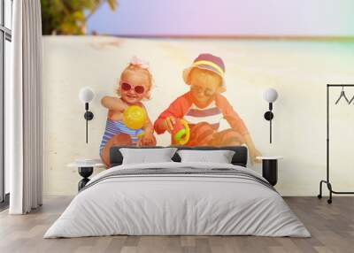 cute little boy and toddler girl play with sand on beach Wall mural