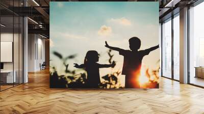 little boy and girl silhouettes play at sunset Wall mural