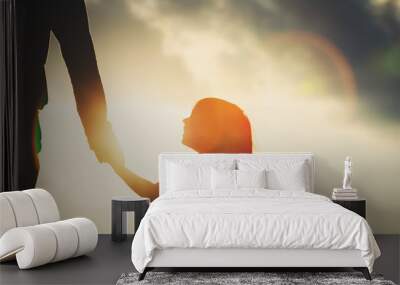 silhouette of little girl holding parent hand at sunset Wall mural