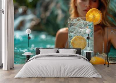  a woman sitting in a pool with a glass of water and lemon slices on the rim of the glass, with a waterfall in the back ground, and a waterfall in the background. Wall mural