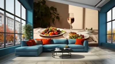  two plates of food and a glass of wine on a table with a white table cloth and a plant in the background. Wall mural