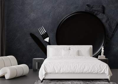 Black plate, cutlery and napkin on stone table top view. Wall mural