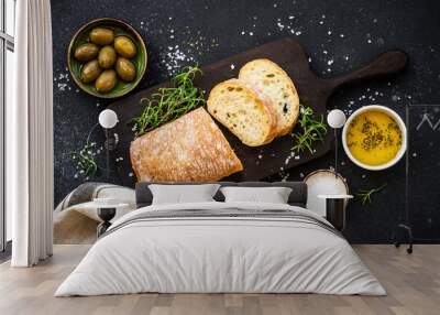 Ciabatta bread with olive oil, olives and herbs on black. Mediterranean food. Top view. Wall mural