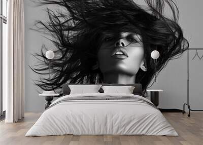 Black and white portrait of a woman with flowing hair in motion, capturing a dramatic and powerful expression. The image highlights contrast and texture. Wall mural