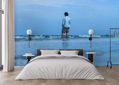 Back view of a young man standing against the sea wave. Feeling of freedom, a male person enjoying sea wave alone. Wall mural