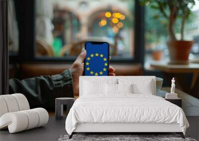 person in cafe holding phone displaying european flag for europe day social media search Wall mural