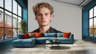 portrait of attractive young man with wavy blonde hair wearing formal attire standing against light grey background Wall mural