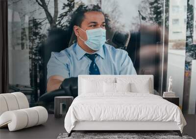 prevent the spread of coronavirus. young hispanic bus driver wearing a protective mask and looks at road. Wall mural