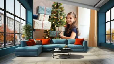 a young girl is surrounded by an abundance of colorful gift boxes, each wrapped in festive paper and ribbons. She holds several large boxes in her arms, her face beaming with excitement and joy Wall mural