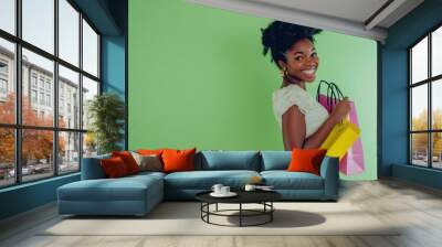 Portrait photo of a happy young african woman with shopping bags in her hand standing on a green background in the right corner of the frame studio light studio photo Wall mural