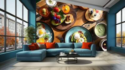 An overhead view of a rustic wooden table set with a delicious brunch spread, including avocado toast, poached eggs, fresh fruit, and artisanal pastries. Wall mural