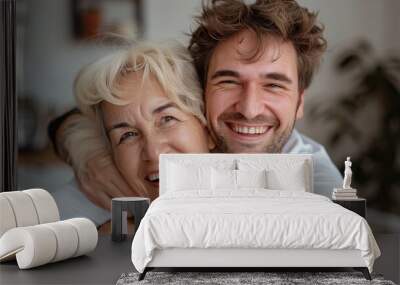 Cheerful caring adult son hugging happy blonde senior mother with love, support, looking at camera with perfect toothy smile, laughing. Wall mural