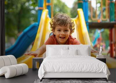 Happy preschooler boy playing on a slide on the playground in summer. copy space for text. Wall mural