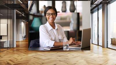 Beautiful young black woman smiling at camera while seated behind her personal computer, where she was working on managing her finances for the upcoming tax period and making online payments. Wall mural