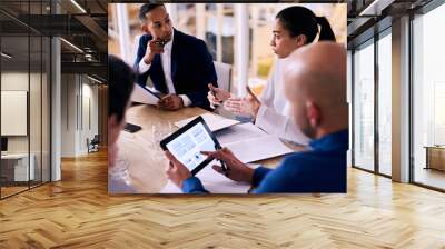 Diverse group of four business individuals listening to a young female partner busy talking to them while looking up the figures she is referring to on his electronic tablet in real time. Wall mural