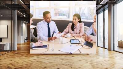 four business professionals conducting a meeting in a bright modern conference room with a large win Wall mural