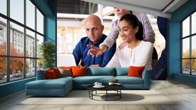 Square image of a diverse group of business individuals busy looking at the latest stock market trends on a laptop screen to see if the can spot patterns together. Wall mural