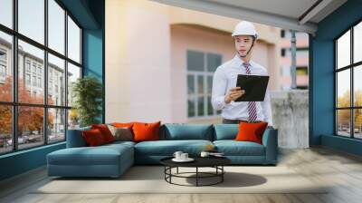  A handsome young engineer stands tall and holds a document. Wall mural