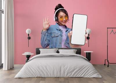 Beautiful Asian teen woman holding smartphone mockup of blank screen and shows ok sign on pink background. Wall mural