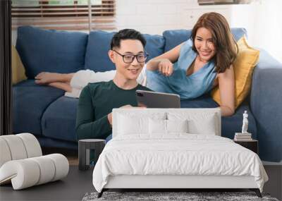 Excited Asian couple man and woman using tablet together on sofa at home. family lifestyle concept. Wall mural