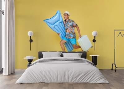 Full body young traveler tourist asian man in summer clothes hat hold suitcase inflatable mattress run isolated on yellow background. Wall mural