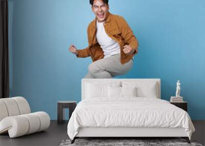 Handsome young Asian man jumping in air very happy and excited, doing winner isolated on blue background. Celebration concept Wall mural