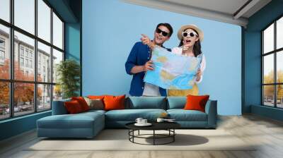 Happy Asian couple tourist looking map and hand pointing to copy space with baggage going to travel on holidays isolated on blue  background. Wall mural